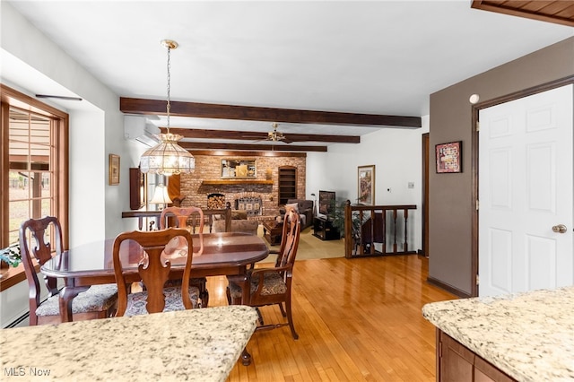 dining space featuring a wall mounted air conditioner, ceiling fan, beam ceiling, a fireplace, and light hardwood / wood-style floors