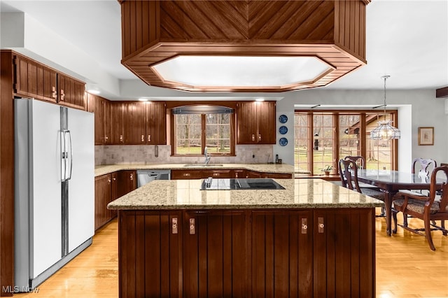 kitchen with decorative light fixtures, white refrigerator, black electric cooktop, and light hardwood / wood-style floors