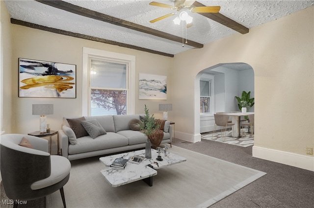 carpeted living room featuring ceiling fan, beam ceiling, and a textured ceiling