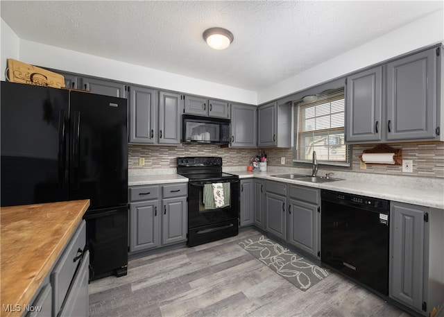 kitchen with gray cabinetry, black appliances, sink, light hardwood / wood-style flooring, and decorative backsplash