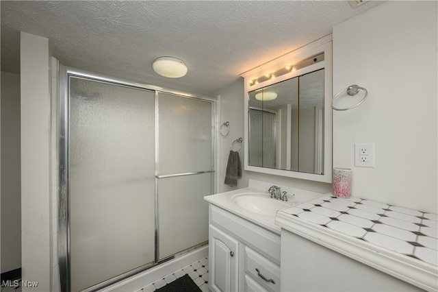 bathroom featuring a textured ceiling, vanity, and a shower with shower door