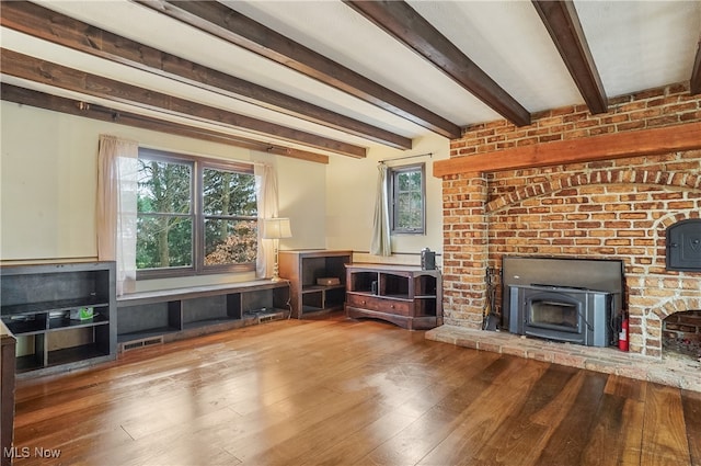 unfurnished living room featuring beam ceiling, wood-type flooring, and a wood stove