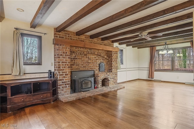 unfurnished living room featuring ceiling fan with notable chandelier, beam ceiling, light wood-type flooring, and a wood stove