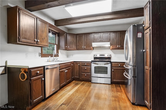 kitchen with appliances with stainless steel finishes, light wood-type flooring, dark brown cabinets, sink, and beamed ceiling