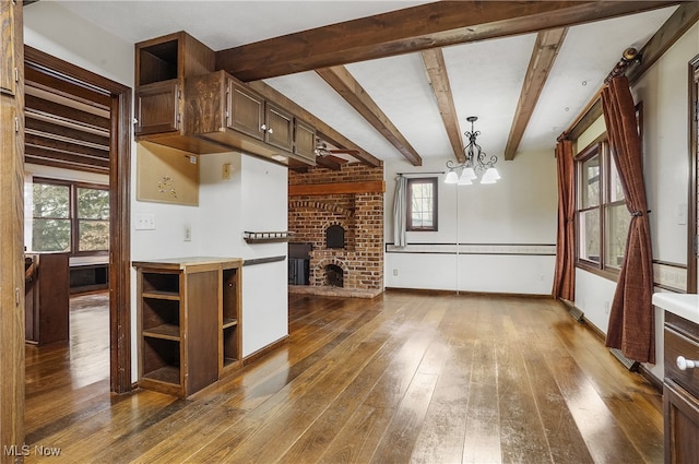 kitchen featuring dark wood-type flooring, an inviting chandelier, a brick fireplace, beamed ceiling, and decorative light fixtures