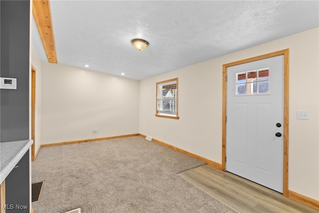 entrance foyer featuring beam ceiling, a textured ceiling, light hardwood / wood-style floors, and a wealth of natural light