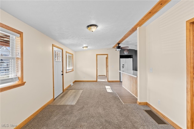 corridor featuring beam ceiling, light carpet, and a textured ceiling