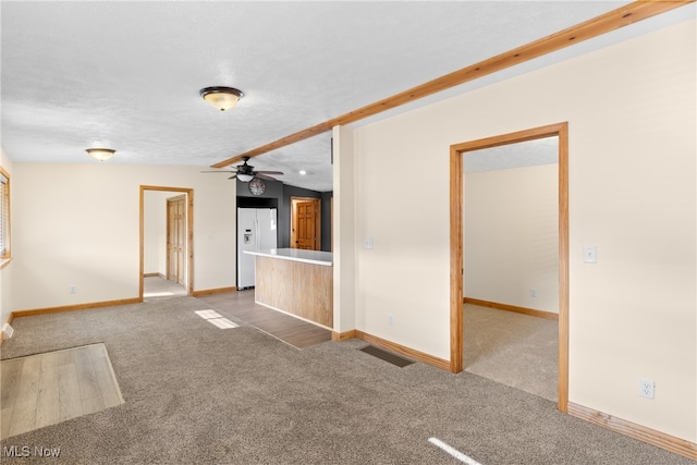 unfurnished living room featuring beamed ceiling, ceiling fan, light colored carpet, and a textured ceiling