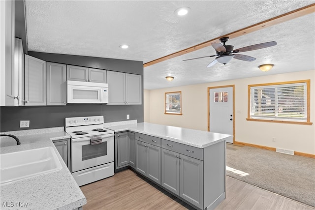 kitchen with kitchen peninsula, a textured ceiling, lofted ceiling, white appliances, and light wood-type flooring