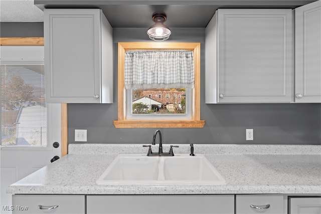 kitchen with white cabinetry, sink, and light stone countertops