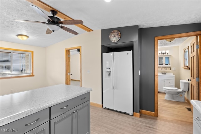 kitchen with gray cabinetry, ceiling fan, white fridge with ice dispenser, light hardwood / wood-style floors, and a textured ceiling