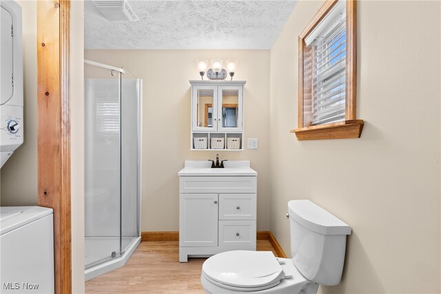 bathroom featuring hardwood / wood-style floors, vanity, a textured ceiling, an enclosed shower, and stacked washer / dryer