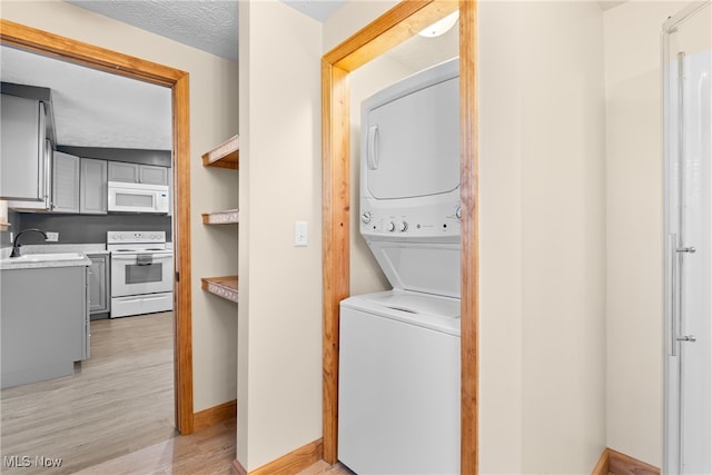 laundry area featuring sink, stacked washing maching and dryer, a textured ceiling, and light wood-type flooring