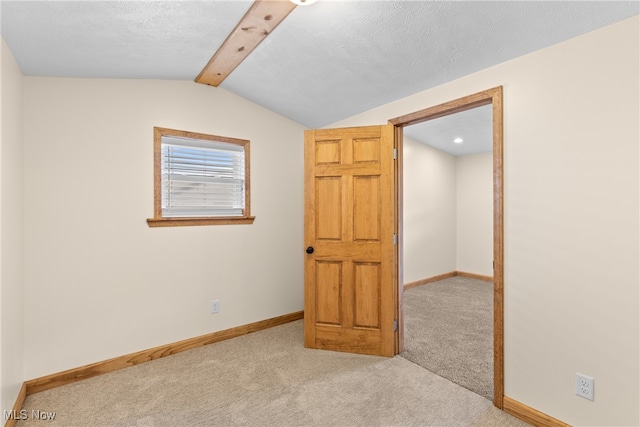 carpeted empty room with lofted ceiling with beams and a textured ceiling