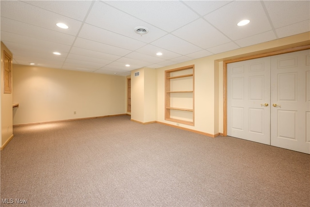 basement featuring carpet flooring, a paneled ceiling, and built in features