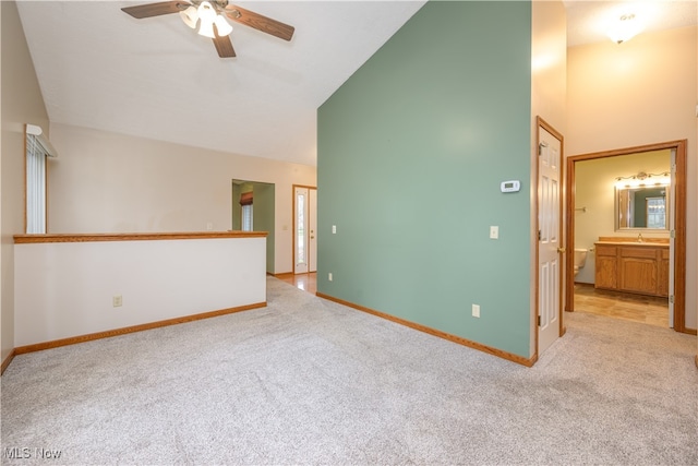 empty room featuring light carpet, sink, ceiling fan, and high vaulted ceiling