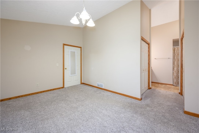 unfurnished room featuring high vaulted ceiling, light colored carpet, and an inviting chandelier