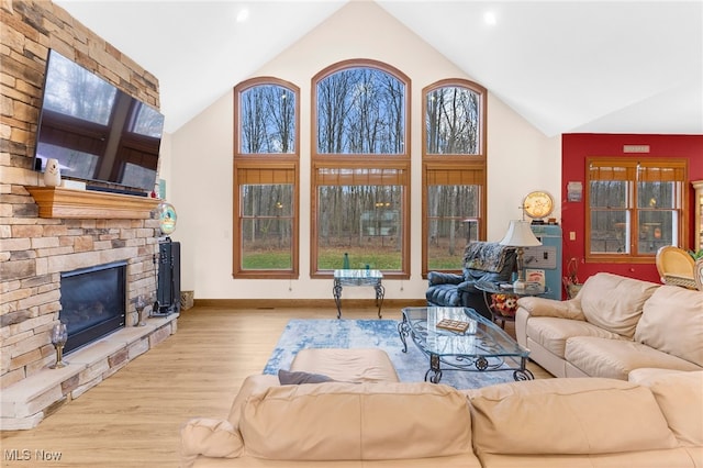 living room with a stone fireplace, high vaulted ceiling, and light hardwood / wood-style floors