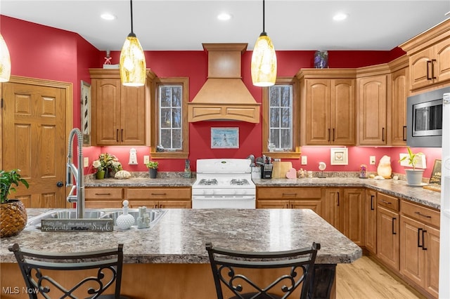 kitchen with custom range hood, white range, stainless steel microwave, and a breakfast bar area