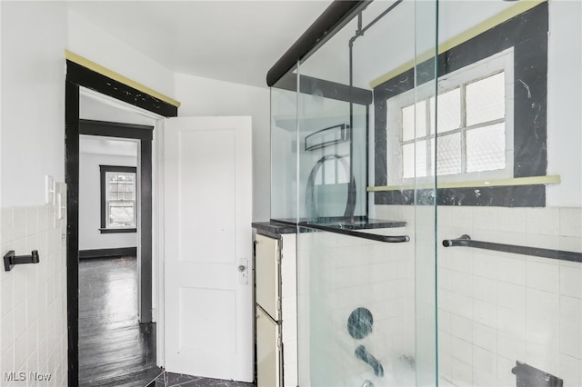 bathroom with shower / bath combination with glass door, hardwood / wood-style flooring, and tile walls