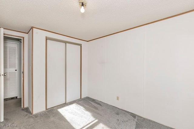 unfurnished bedroom featuring light carpet, a textured ceiling, a closet, and ornamental molding