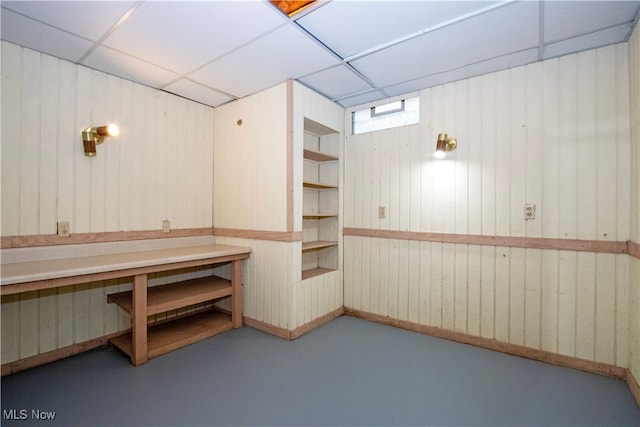 basement featuring a drop ceiling and wooden walls