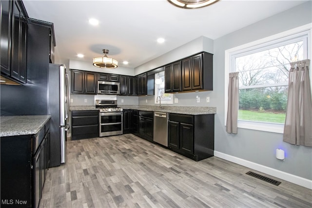 kitchen with light stone countertops, appliances with stainless steel finishes, light wood-type flooring, and sink