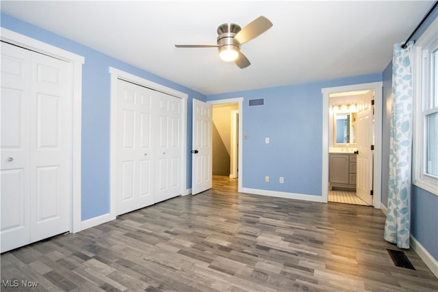 unfurnished bedroom featuring dark hardwood / wood-style floors, ceiling fan, ensuite bathroom, and two closets