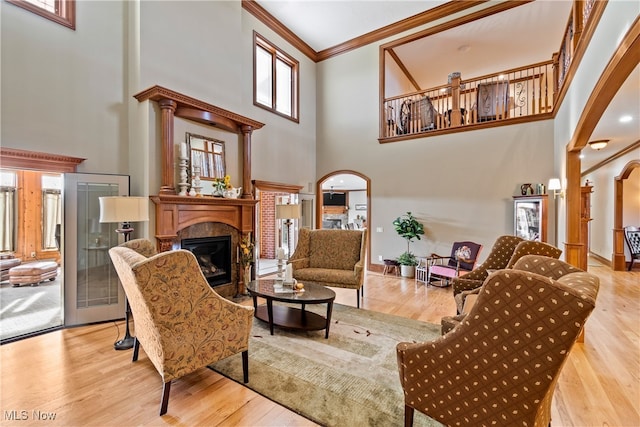 living room featuring a high ceiling, light wood-type flooring, decorative columns, and crown molding