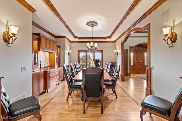 dining room featuring light wood-type flooring, a tray ceiling, crown molding, and a notable chandelier