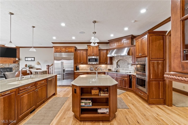 kitchen featuring built in appliances, pendant lighting, light wood-type flooring, and an island with sink