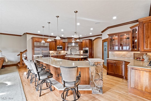 kitchen with light wood-type flooring, pendant lighting, built in appliances, and a spacious island