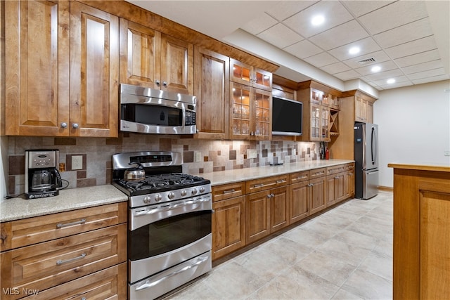 kitchen with a paneled ceiling, decorative backsplash, light stone countertops, light tile patterned flooring, and stainless steel appliances