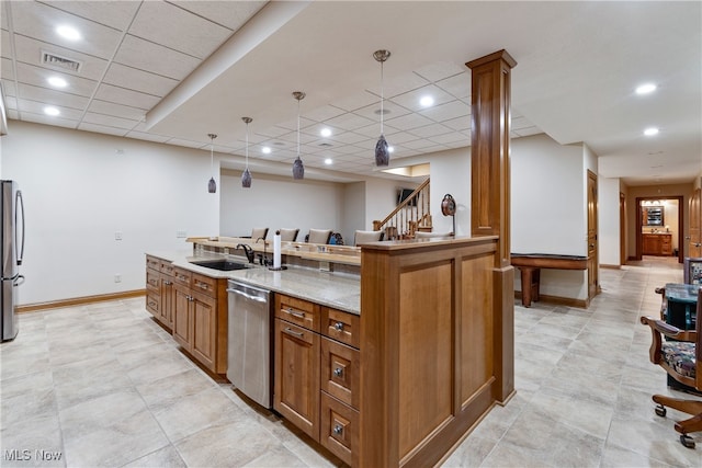 kitchen featuring light stone countertops, appliances with stainless steel finishes, sink, a center island with sink, and decorative light fixtures