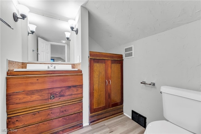 bathroom featuring wood-type flooring, vanity, toilet, and lofted ceiling