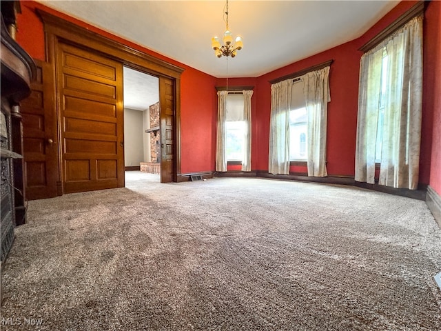 carpeted spare room with a notable chandelier and a brick fireplace