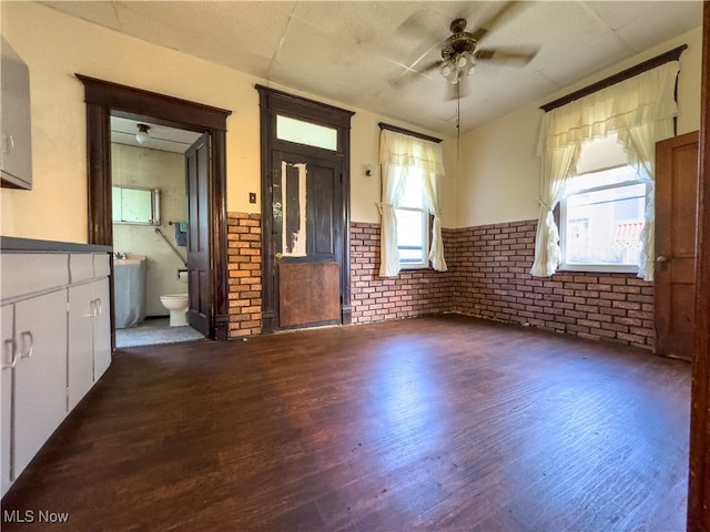 unfurnished living room with ceiling fan, brick wall, and dark hardwood / wood-style floors