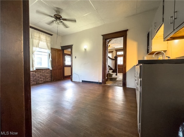 unfurnished room with ceiling fan, dark wood-type flooring, and brick wall