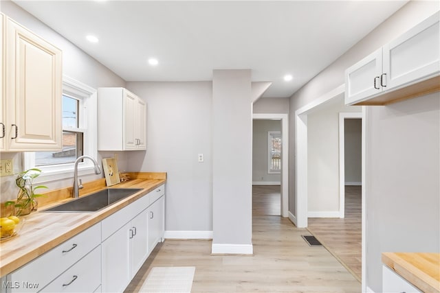 kitchen featuring butcher block countertops, white cabinetry, and light hardwood / wood-style flooring