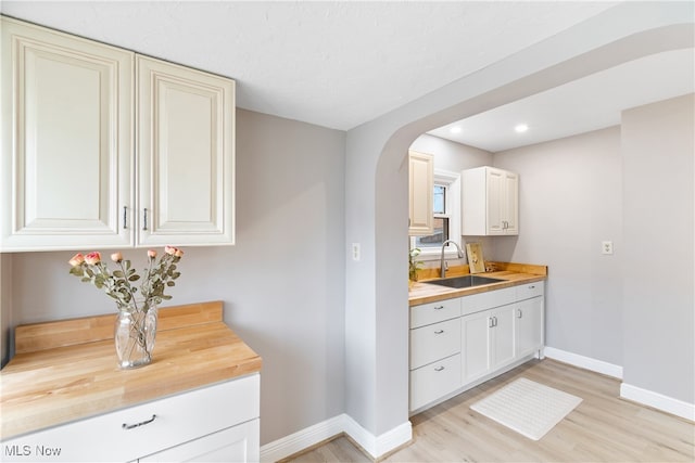 interior space featuring butcher block counters, light wood-type flooring, sink, and white cabinetry