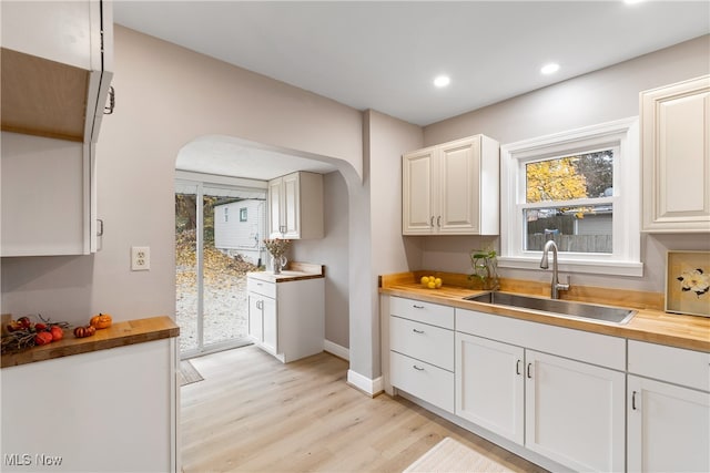 kitchen featuring butcher block countertops, white cabinetry, sink, and light hardwood / wood-style floors