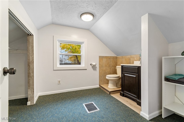 bathroom with a textured ceiling, vanity, toilet, and vaulted ceiling