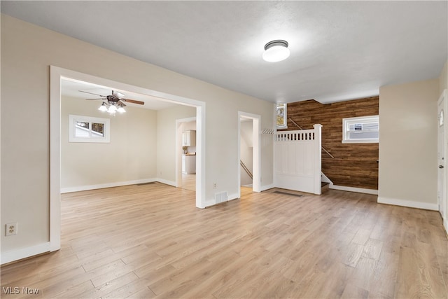 spare room with ceiling fan, light wood-type flooring, and wooden walls