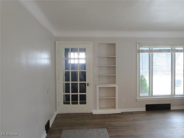 spare room with dark hardwood / wood-style floors, a healthy amount of sunlight, and built in features