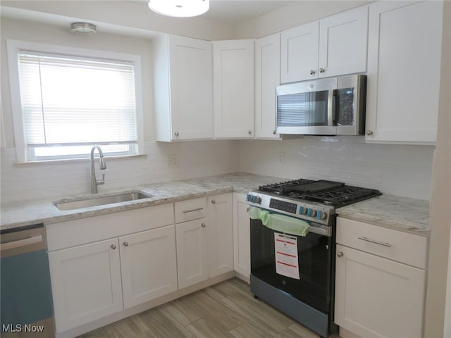 kitchen featuring light stone countertops, white cabinetry, sink, stainless steel appliances, and tasteful backsplash