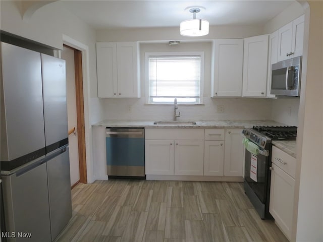 kitchen featuring light stone counters, stainless steel appliances, sink, white cabinets, and light hardwood / wood-style floors