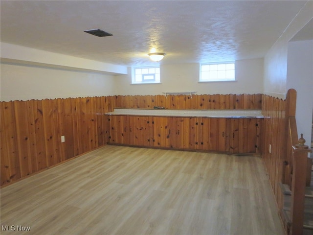 basement featuring wood walls, a textured ceiling, and light wood-type flooring