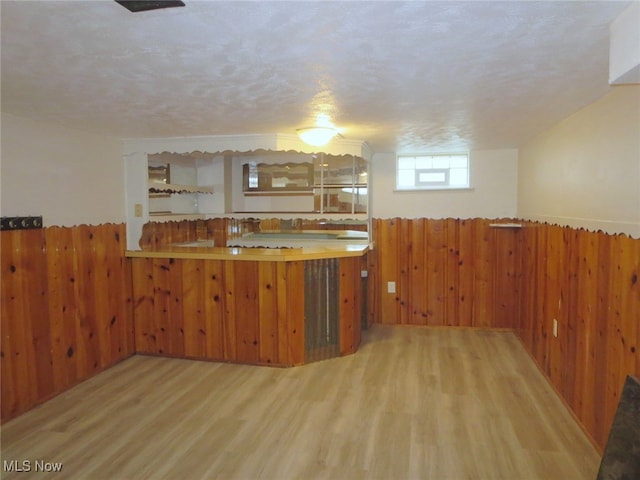 kitchen featuring kitchen peninsula, wooden walls, light hardwood / wood-style floors, and a textured ceiling