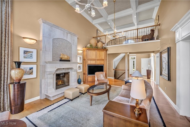 living room with coffered ceiling, a high ceiling, a chandelier, a fireplace, and light wood-type flooring