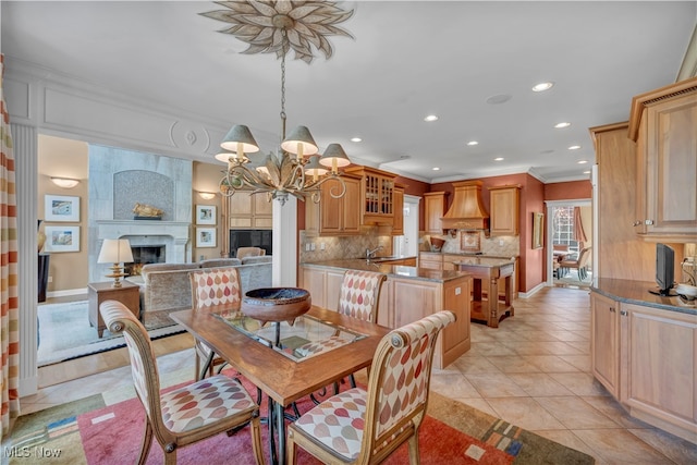 dining room featuring sink, ornamental molding, light tile patterned floors, a large fireplace, and a chandelier